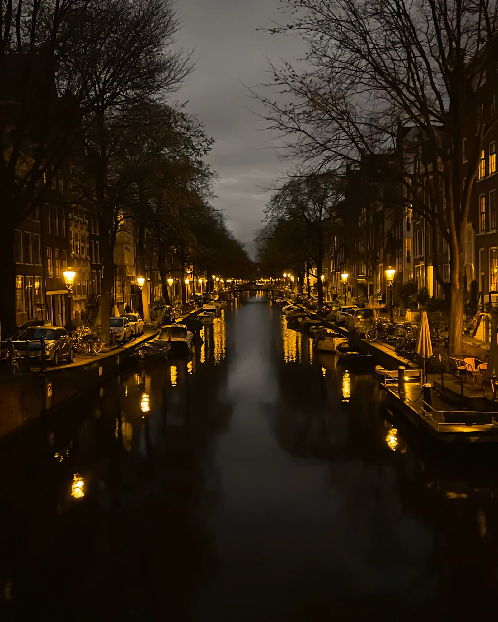An Amsterdam canal at dusk, lit by street lamps