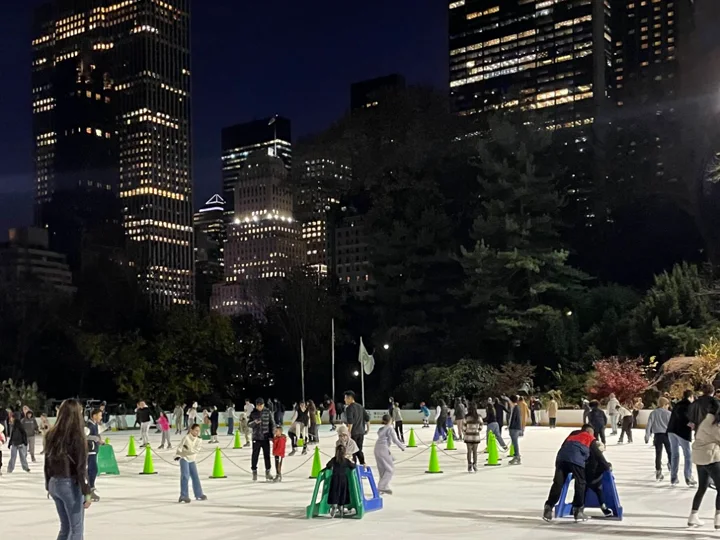 Skaters on Wollman Rink at night under the Central Park South skyline